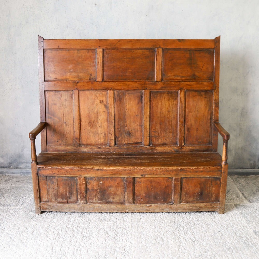 A high-backed antique wooden settle featuring raised timber panels, flat armrests with turned supports, and an enclosed panelled base. View II