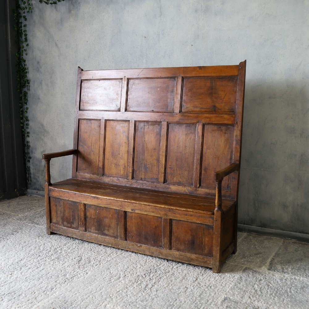 A high-backed antique wooden settle featuring raised timber panels, flat armrests with turned supports, and an enclosed panelled base. View III