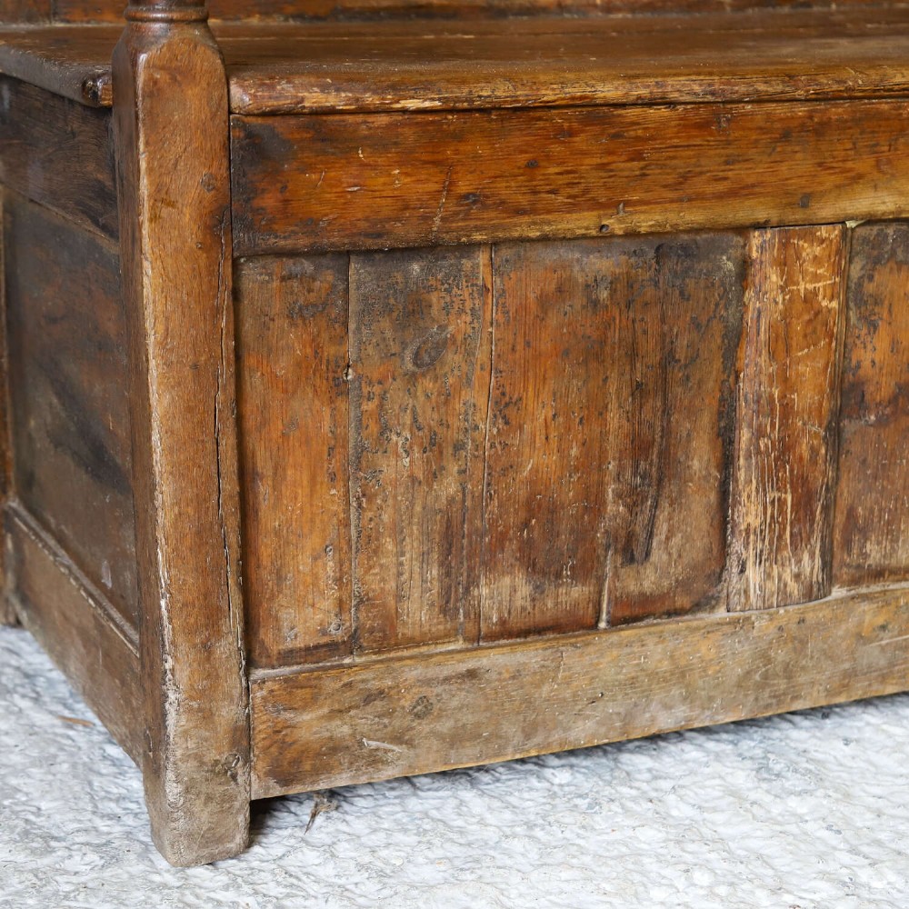 A high-backed antique wooden settle featuring raised timber panels, flat armrests with turned supports, and an enclosed panelled base. View IV