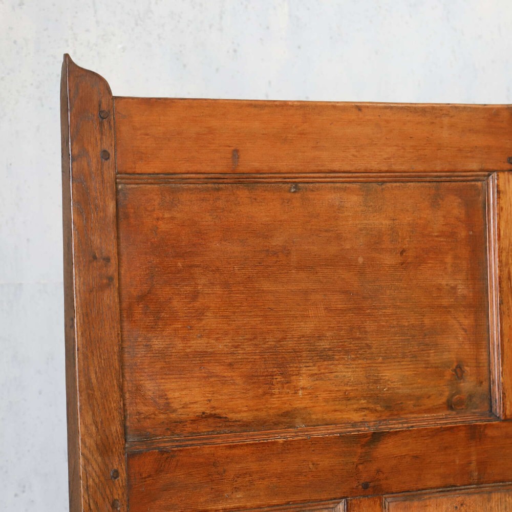 A high-backed antique wooden settle featuring raised timber panels, flat armrests with turned supports, and an enclosed panelled base. View VI