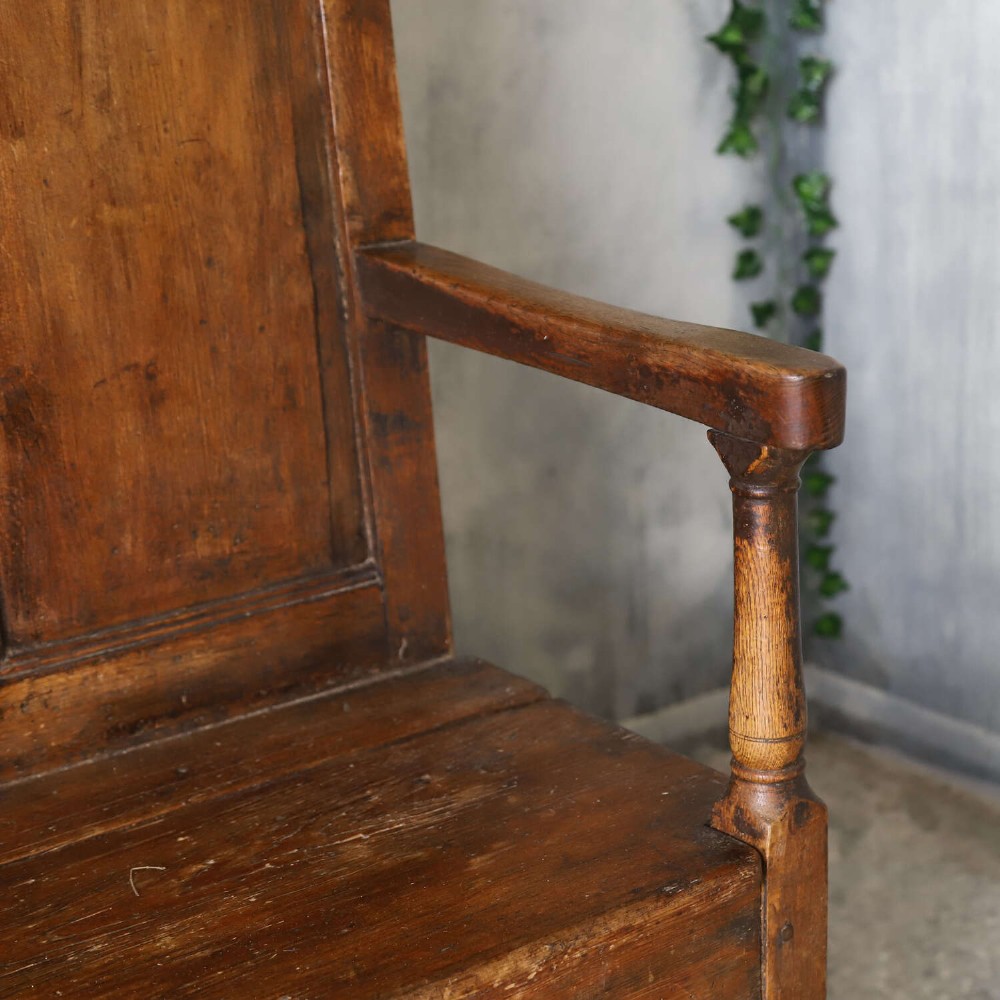A high-backed antique wooden settle featuring raised timber panels, flat armrests with turned supports, and an enclosed panelled base. View VIII