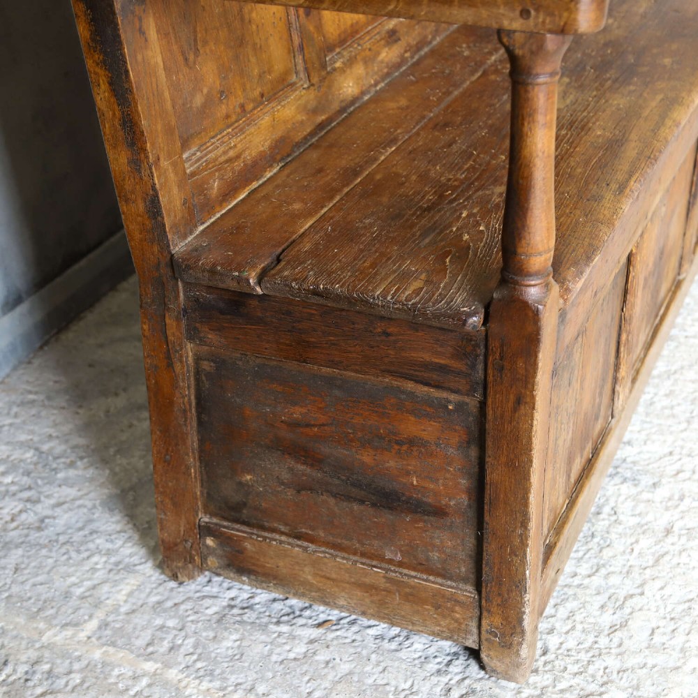 A high-backed antique wooden settle featuring raised timber panels, flat armrests with turned supports, and an enclosed panelled base. View XII