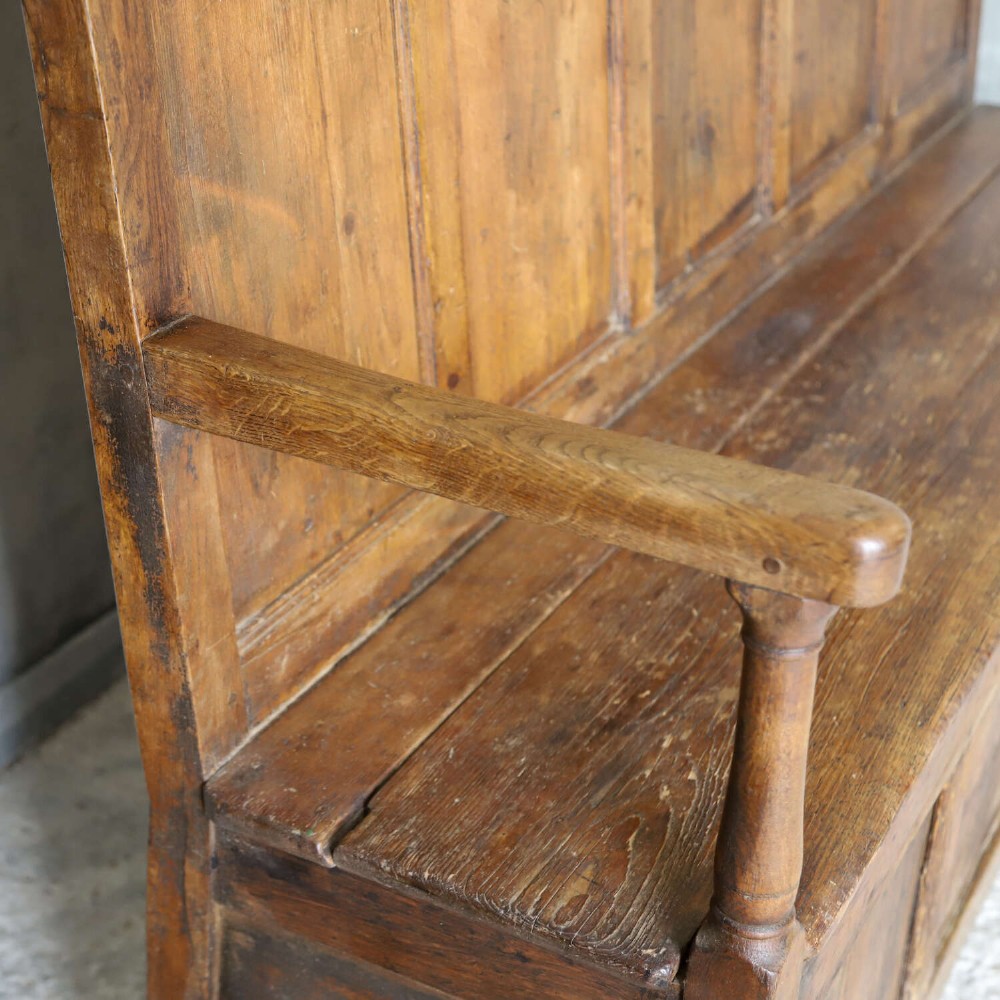 A high-backed antique wooden settle featuring raised timber panels, flat armrests with turned supports, and an enclosed panelled base. View XIII