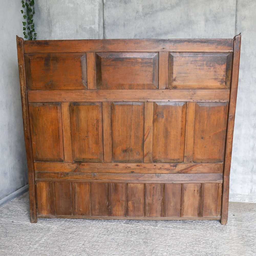 A high-backed antique wooden settle featuring raised timber panels, flat armrests with turned supports, and an enclosed panelled base. View XV