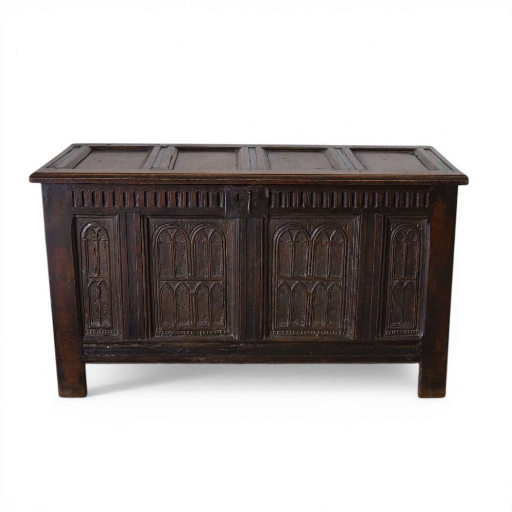 A dark oak coffer featuring four hand-carved Gothic arch panels, a fluted frieze, and a sturdy four-panel hinged lid.