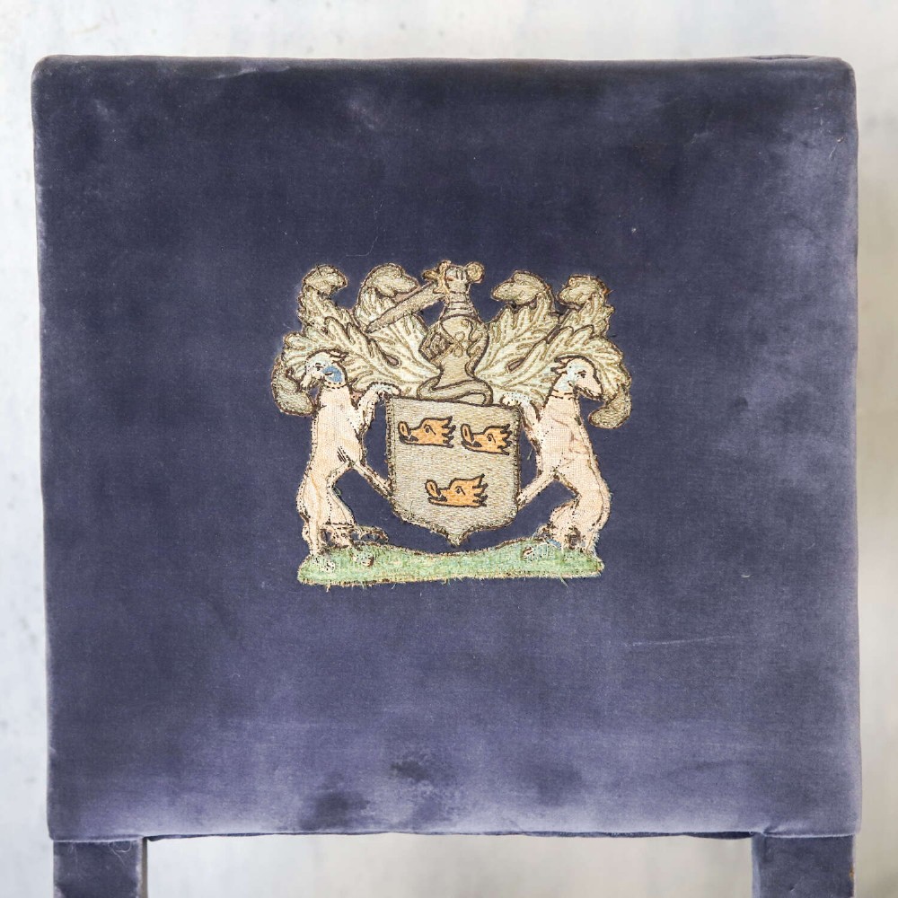 A matched pair of dark oak side chairs upholstered in dark blue velvet, featuring embroidered heraldic crests on the backrests and gold tassel fringe around the seat borders. View V