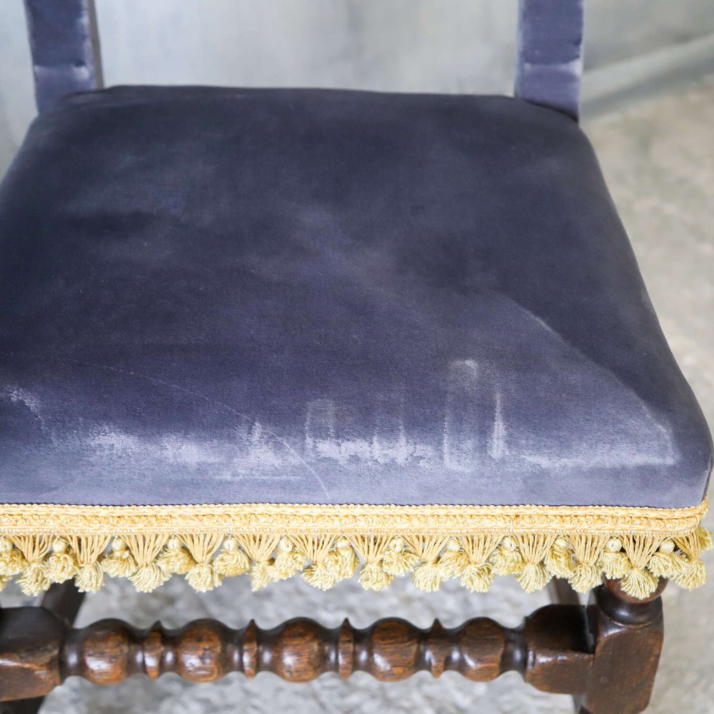 A matched pair of dark oak side chairs upholstered in dark blue velvet, featuring embroidered heraldic crests on the backrests and gold tassel fringe around the seat borders. View VI