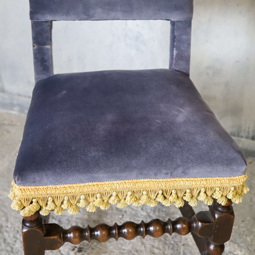 A matched pair of dark oak side chairs upholstered in dark blue velvet, featuring embroidered heraldic crests on the backrests and gold tassel fringe around the seat borders. View VII