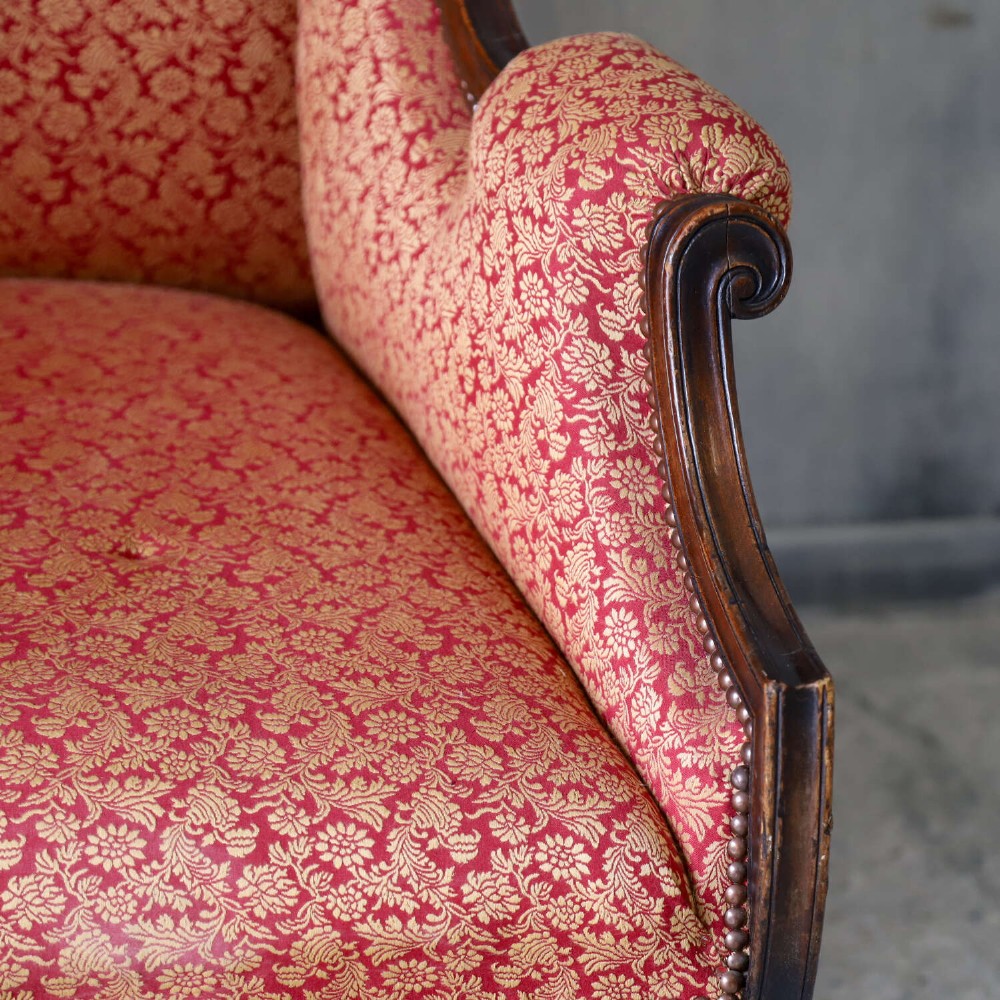 A mid-19th-century high-back wing armchair upholstered in red and gold patterned fabric with carved dark timber legs on casters. View IV