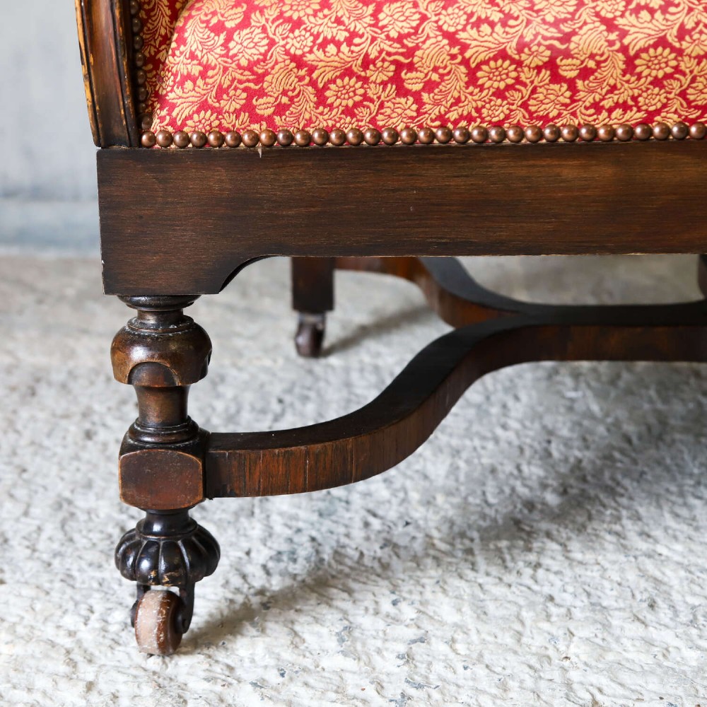 A mid-19th-century high-back wing armchair upholstered in red and gold patterned fabric with carved dark timber legs on casters. View V