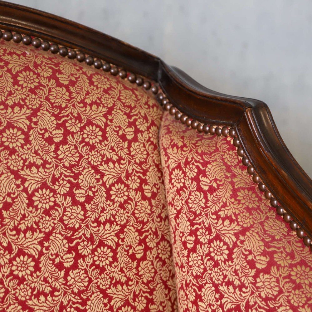 A mid-19th-century high-back wing armchair upholstered in red and gold patterned fabric with carved dark timber legs on casters. View IX