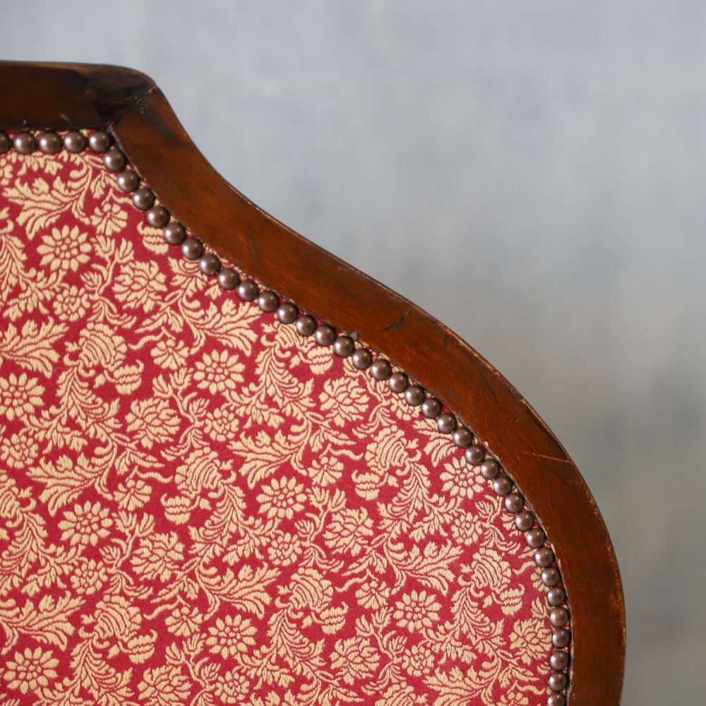 A mid-19th-century high-back wing armchair upholstered in red and gold patterned fabric with carved dark timber legs on casters. View XI