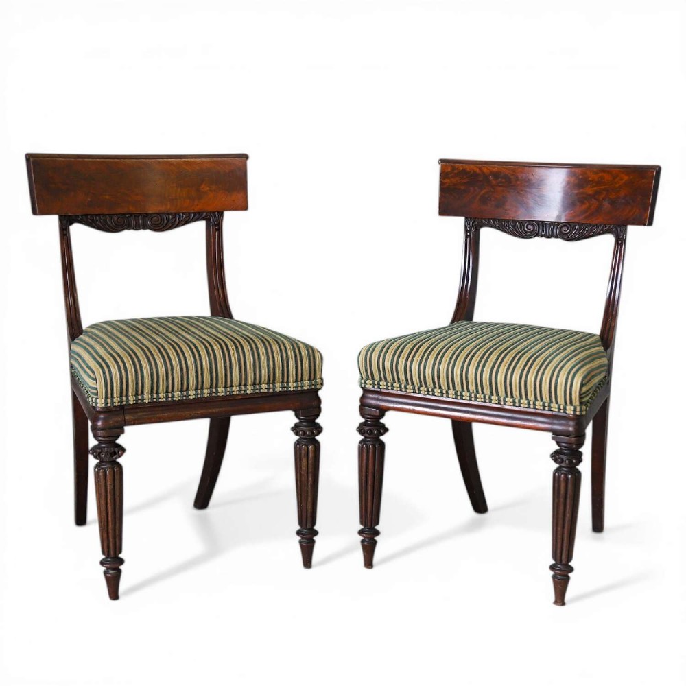 A pair of William IV mahogany side chairs featuring curved top rails with relief carving, fluted front legs, and seats upholstered in green and gold striped fabric.