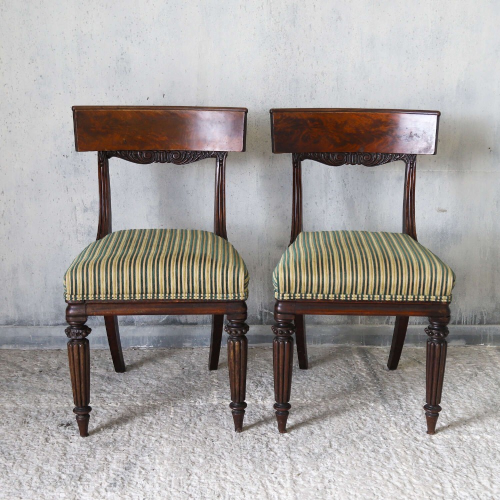 A pair of William IV mahogany side chairs featuring curved top rails with relief carving, fluted front legs, and seats upholstered in green and gold striped fabric. View II
