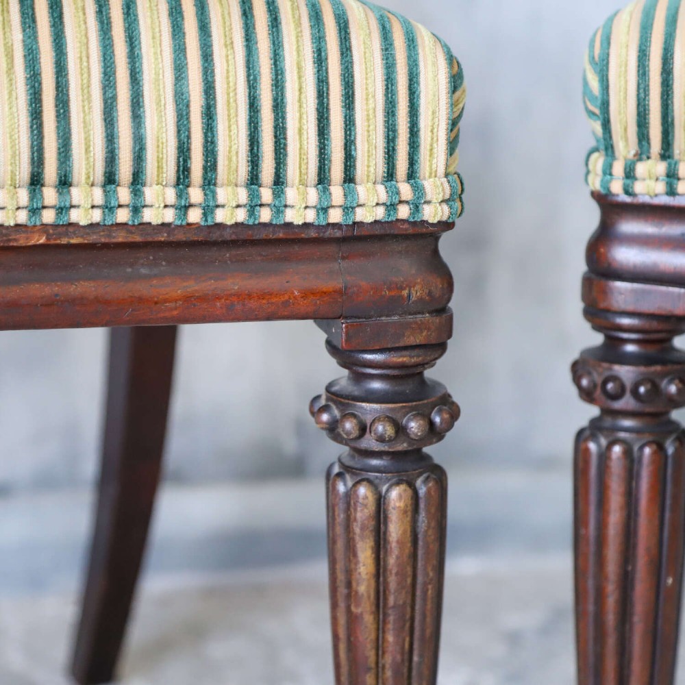 A pair of William IV mahogany side chairs featuring curved top rails with relief carving, fluted front legs, and seats upholstered in green and gold striped fabric. View III