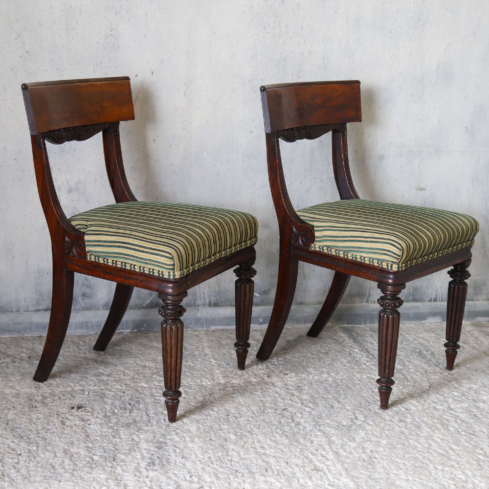 A pair of William IV mahogany side chairs featuring curved top rails with relief carving, fluted front legs, and seats upholstered in green and gold striped fabric. View X