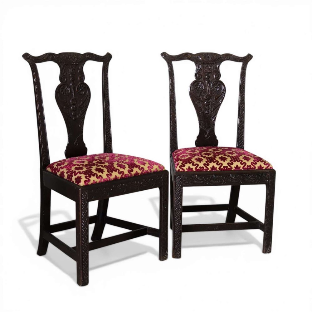 A pair of dark carved oak side chairs with vasiform splats and seats upholstered in red and gold patterned velvet.