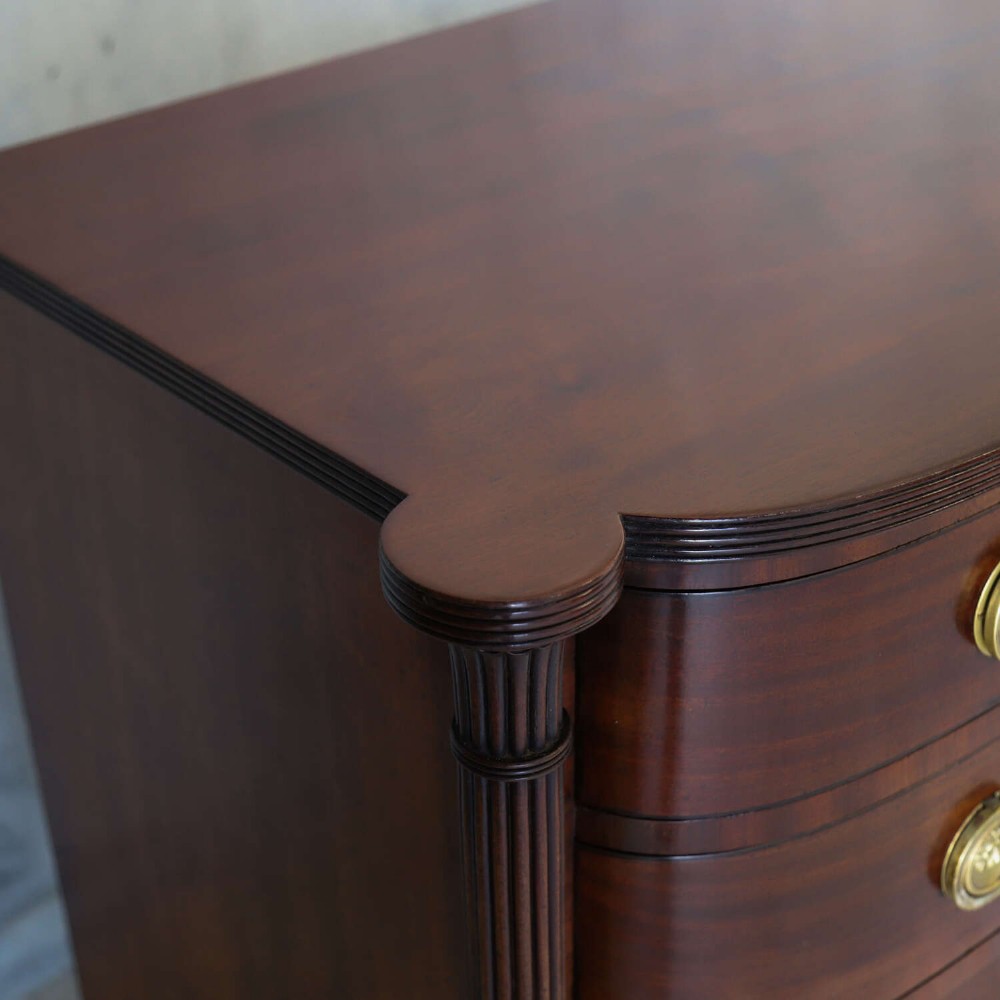 A Scottish Regency flame mahogany bowfront chest of four graduated drawers featuring brass ring handles, reeded side columns, and turned feet. View III