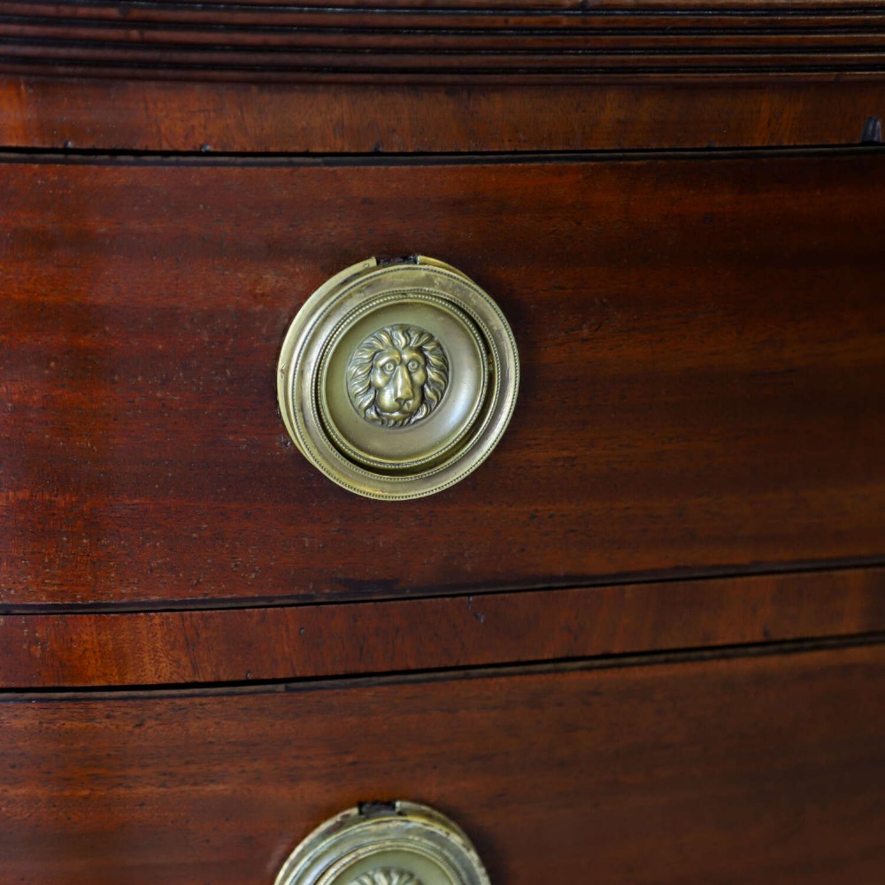 A Scottish Regency flame mahogany bowfront chest of four graduated drawers featuring brass ring handles, reeded side columns, and turned feet. View IV
