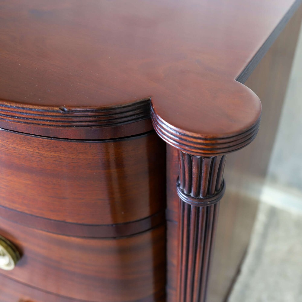 A Scottish Regency flame mahogany bowfront chest of four graduated drawers featuring brass ring handles, reeded side columns, and turned feet. View V