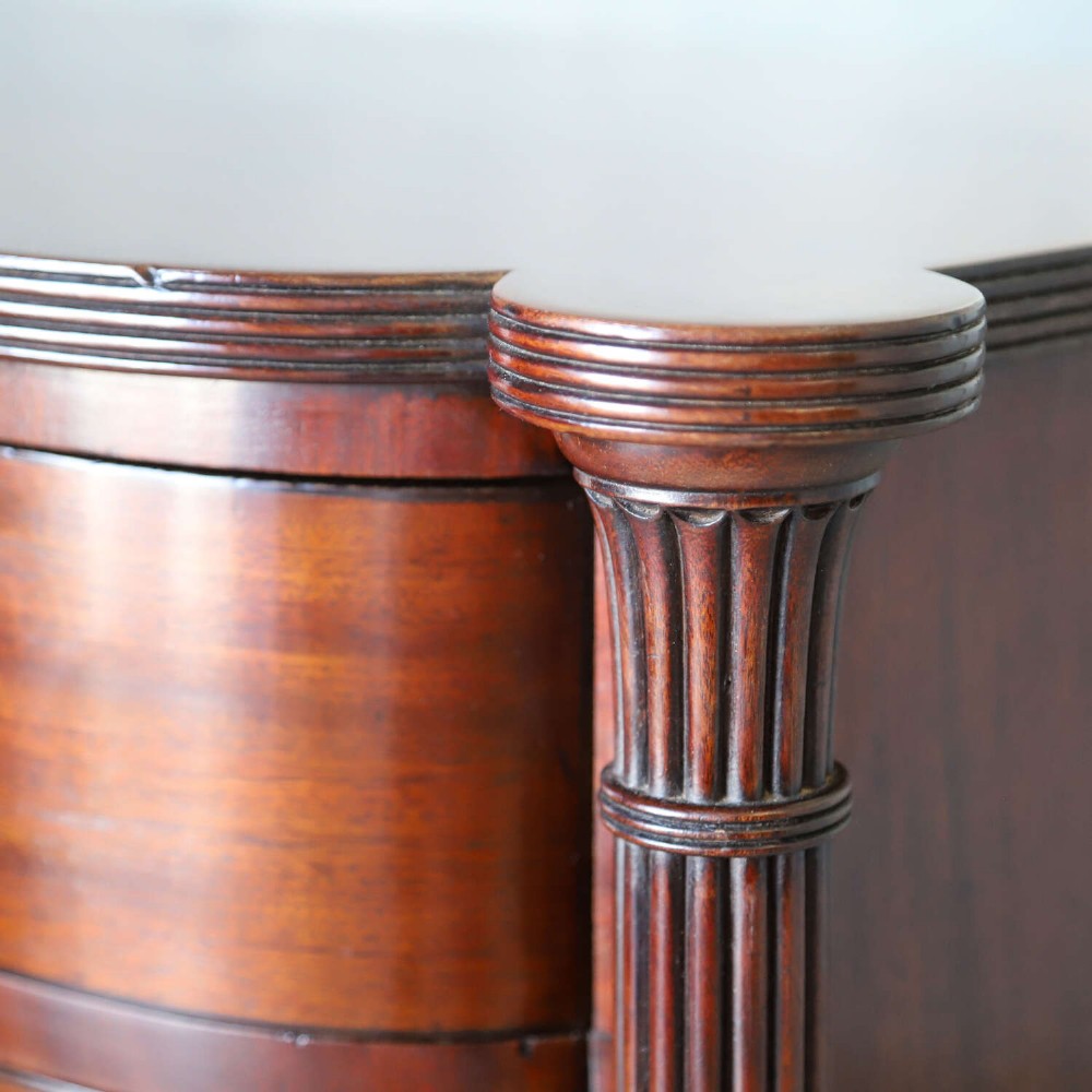 A Scottish Regency flame mahogany bowfront chest of four graduated drawers featuring brass ring handles, reeded side columns, and turned feet. View VII