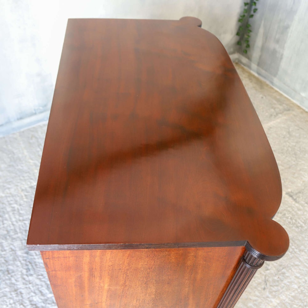 A Scottish Regency flame mahogany bowfront chest of four graduated drawers featuring brass ring handles, reeded side columns, and turned feet. View X