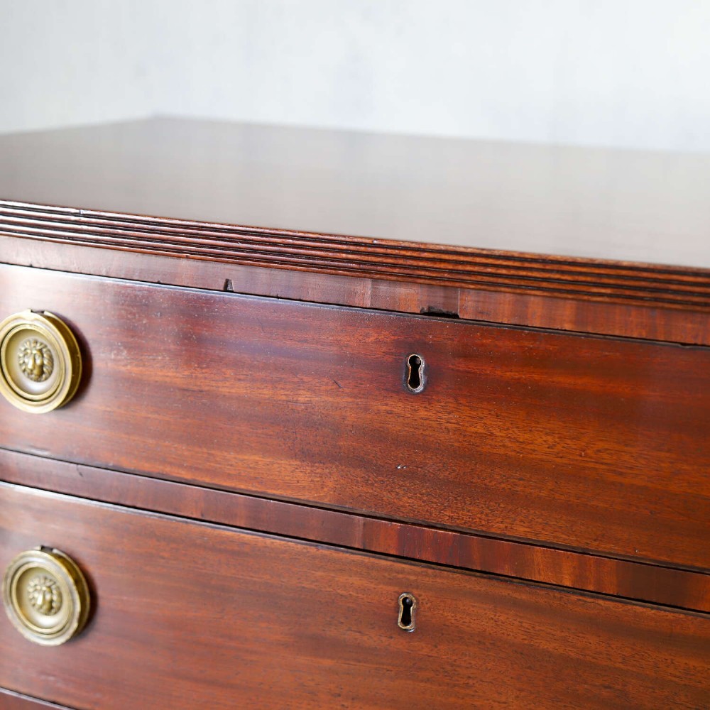A Scottish Regency flame mahogany bowfront chest of four graduated drawers featuring brass ring handles, reeded side columns, and turned feet. View XI