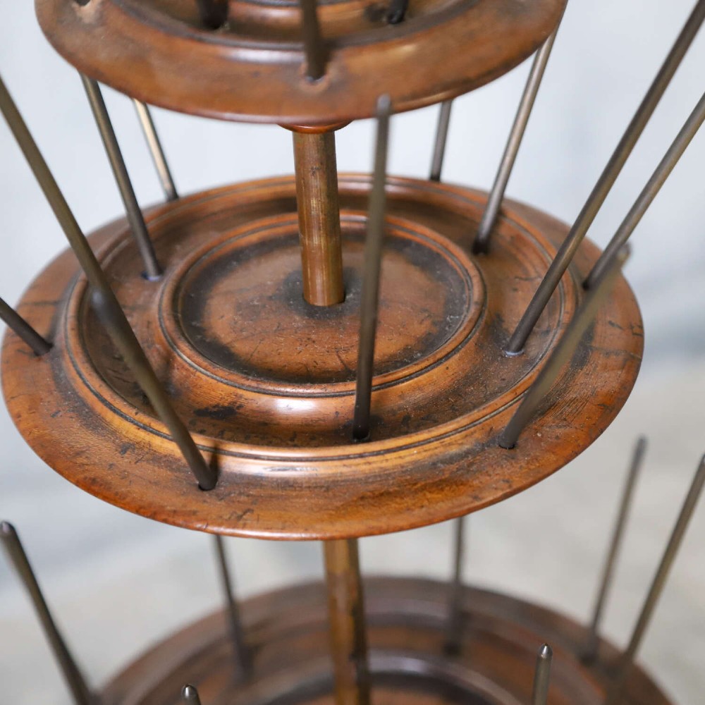 A four-tiered Victorian cotton reel display tree featuring circular wooden tiers with vertical metal spindles set on a cast iron base. View X