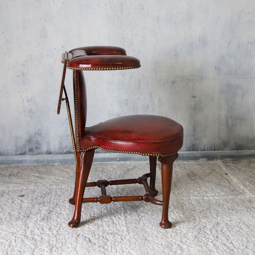 A late Victorian Sheraton style reading chair upholstered in burgundy red leather with brass studding and mahogany legs. View XV