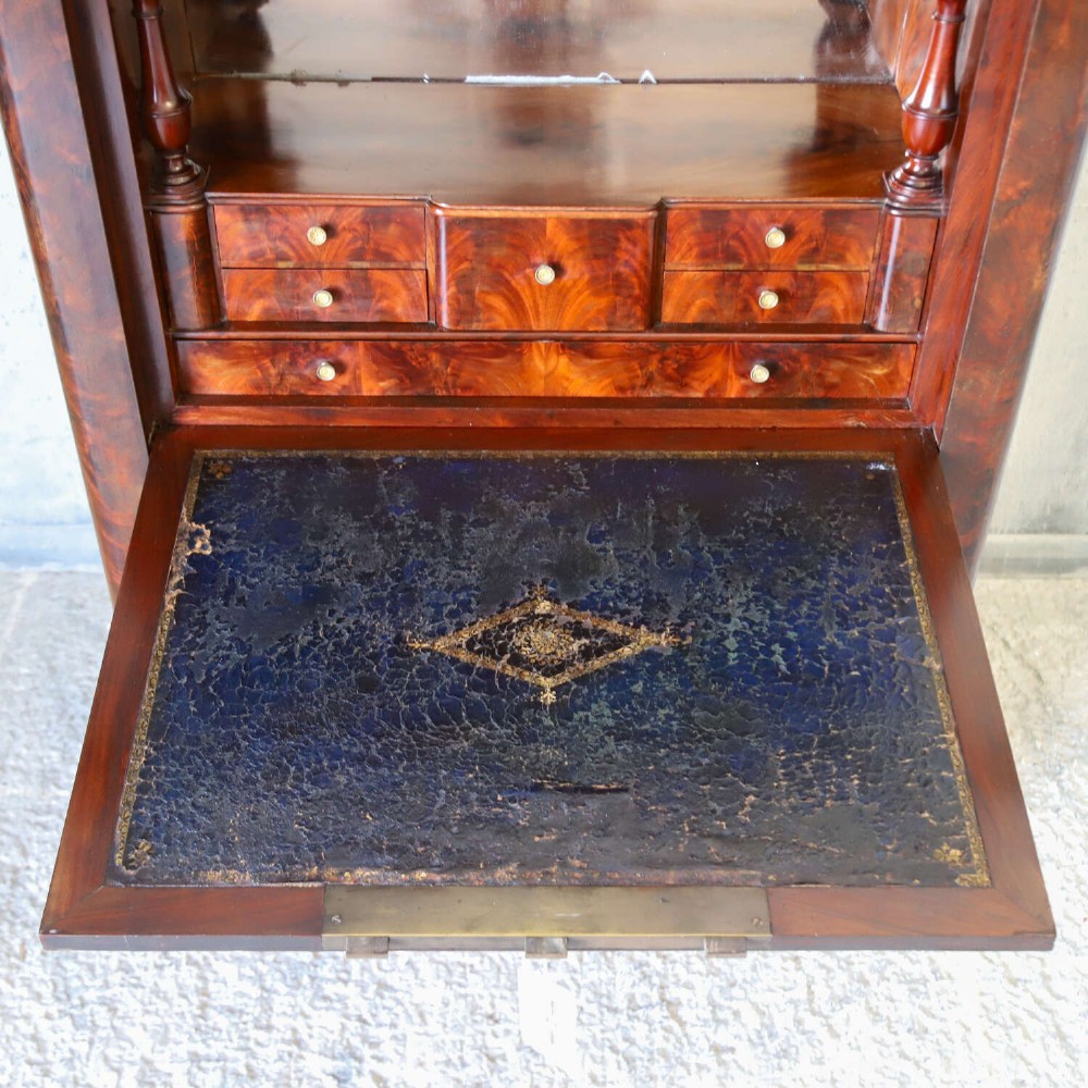 A 19th-century French secretaire a abattant featuring flame mahogany veneers, a dark marble top slab, an upper drop-front writing panel, and lower cupboard doors. View IV