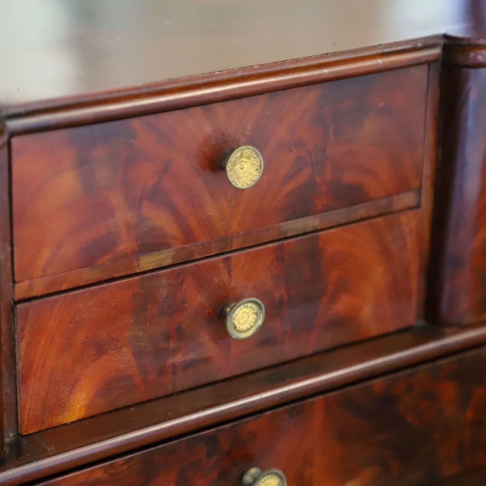 A 19th-century French secretaire a abattant featuring flame mahogany veneers, a dark marble top slab, an upper drop-front writing panel, and lower cupboard doors. View IX