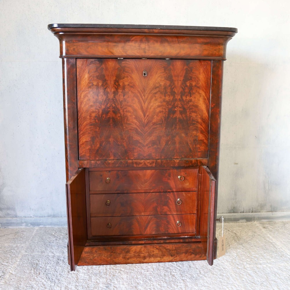 A 19th-century French secretaire a abattant featuring flame mahogany veneers, a dark marble top slab, an upper drop-front writing panel, and lower cupboard doors. View XII