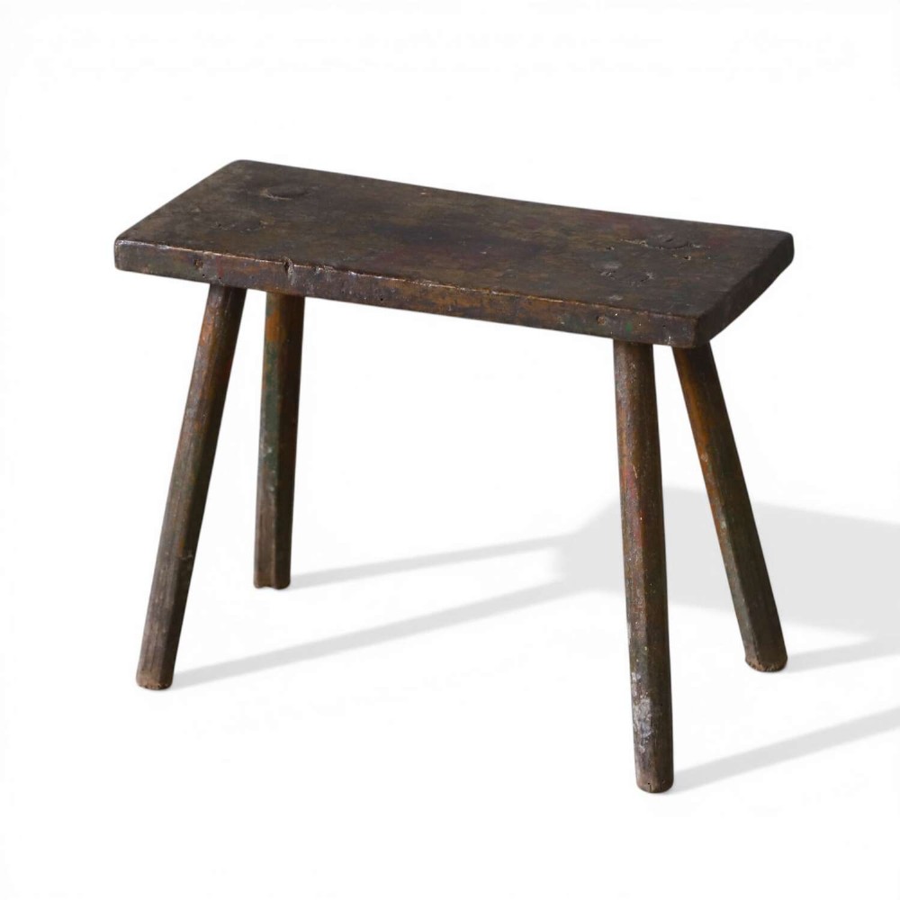 A rectangular rustic wooden milking stool with splayed cylindrical legs and a distressed dark green painted finish.