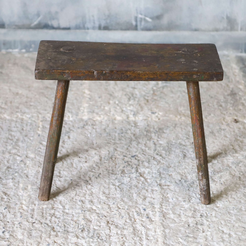 A rectangular rustic wooden milking stool with splayed cylindrical legs and a distressed dark green painted finish. View II