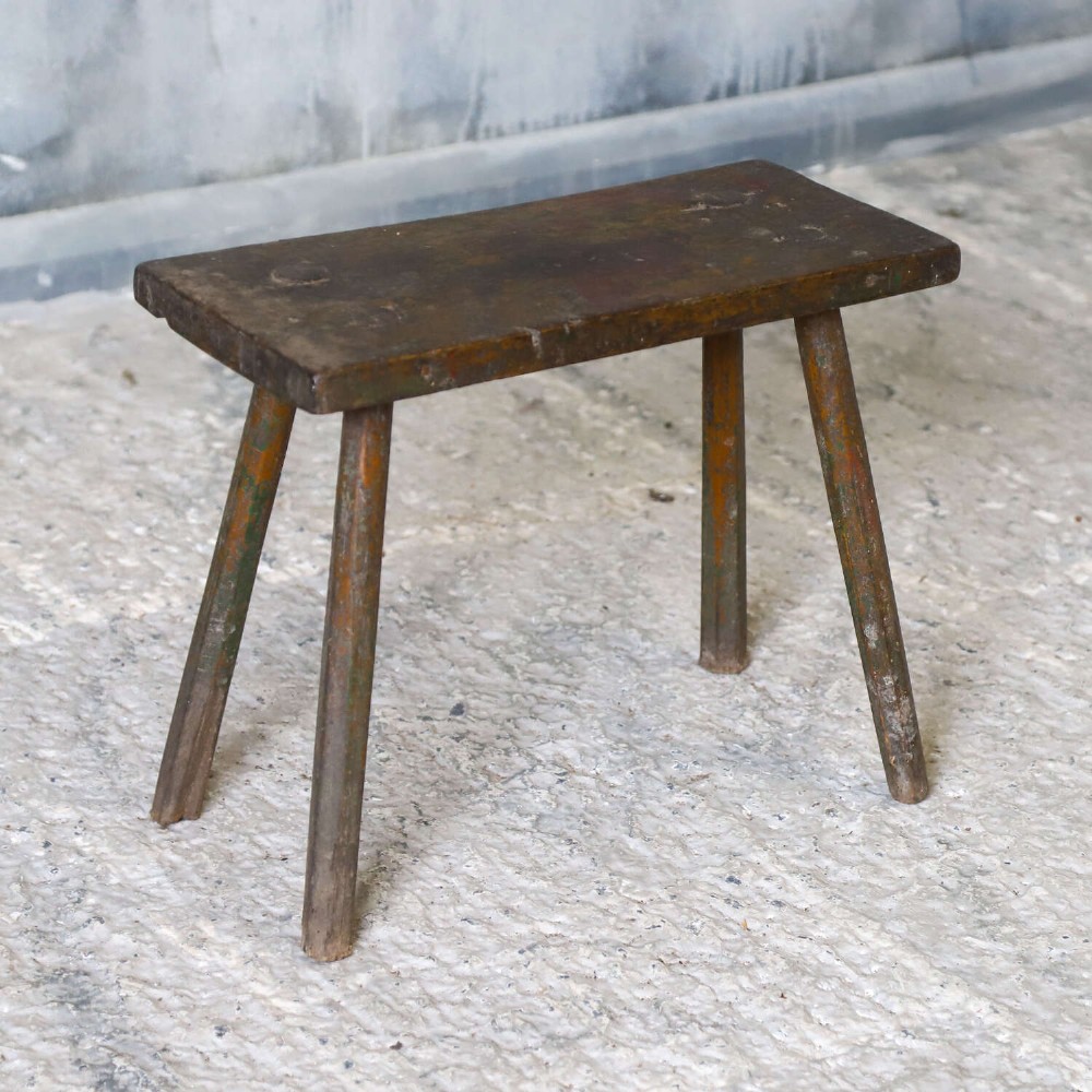A rectangular rustic wooden milking stool with splayed cylindrical legs and a distressed dark green painted finish. View IV