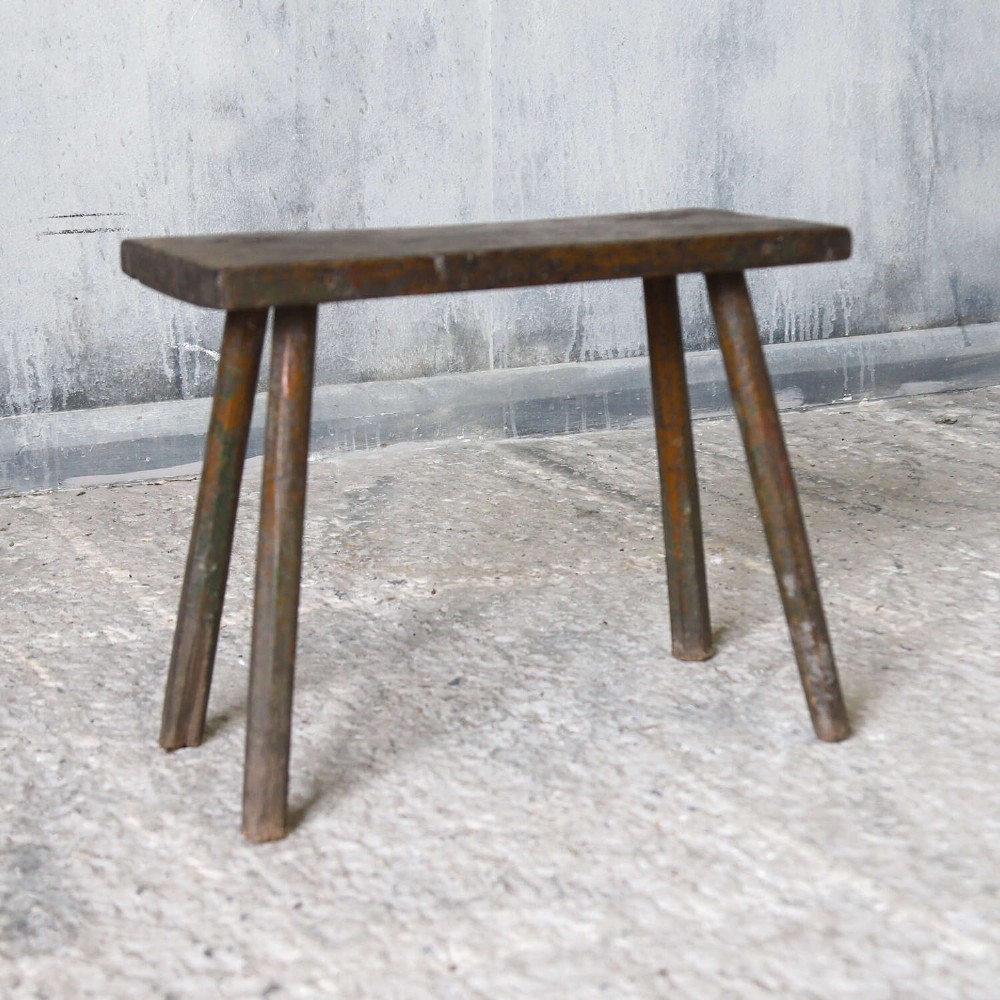 A rectangular rustic wooden milking stool with splayed cylindrical legs and a distressed dark green painted finish. View VI