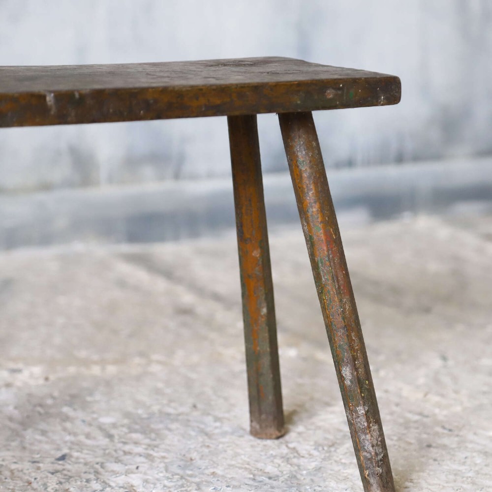 A rectangular rustic wooden milking stool with splayed cylindrical legs and a distressed dark green painted finish. View VII
