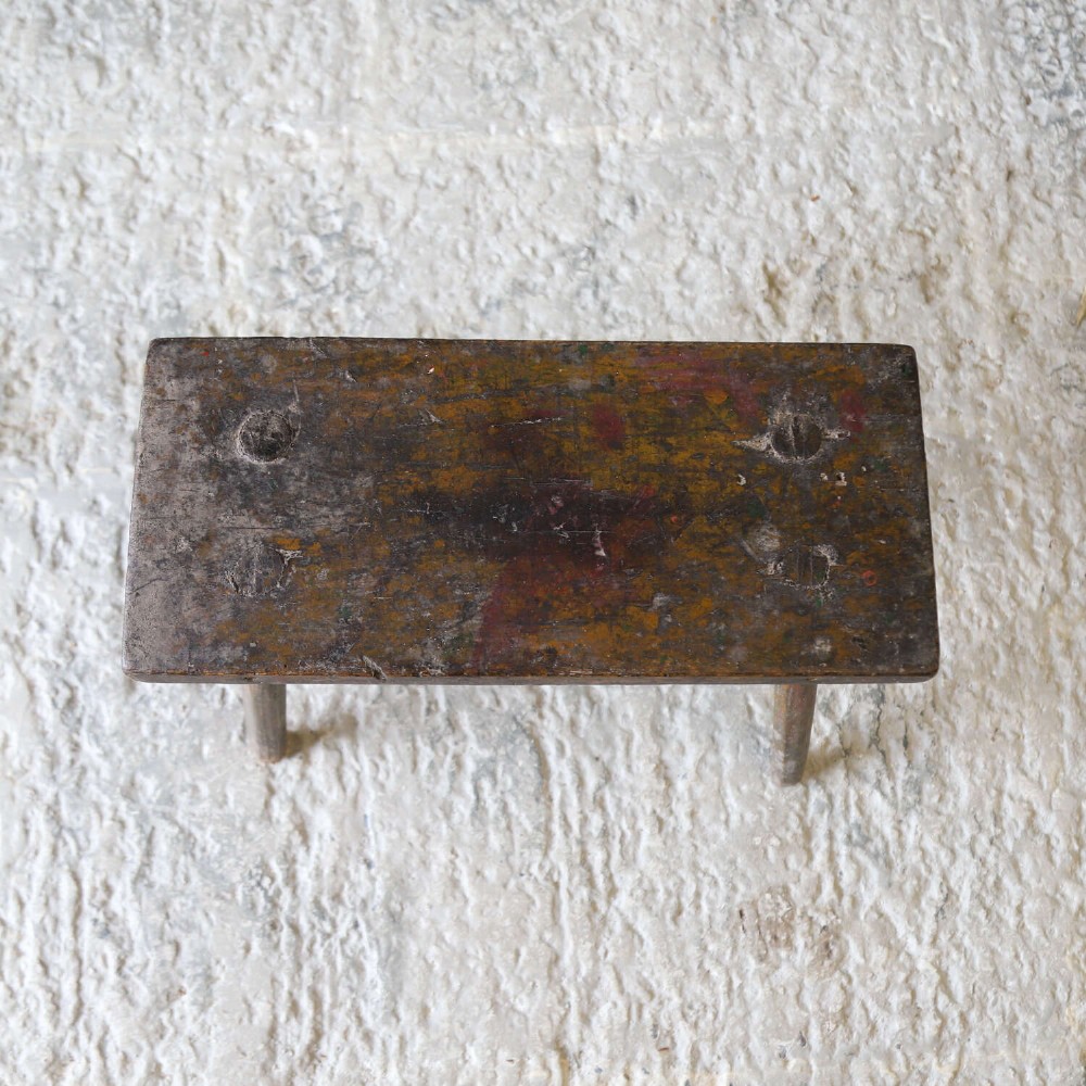 A rectangular rustic wooden milking stool with splayed cylindrical legs and a distressed dark green painted finish. View VIII