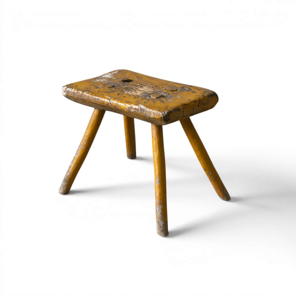 A nineteenth-century rectangular wooden milking stool with four splayed legs and a weathered ochre yellow painted finish.