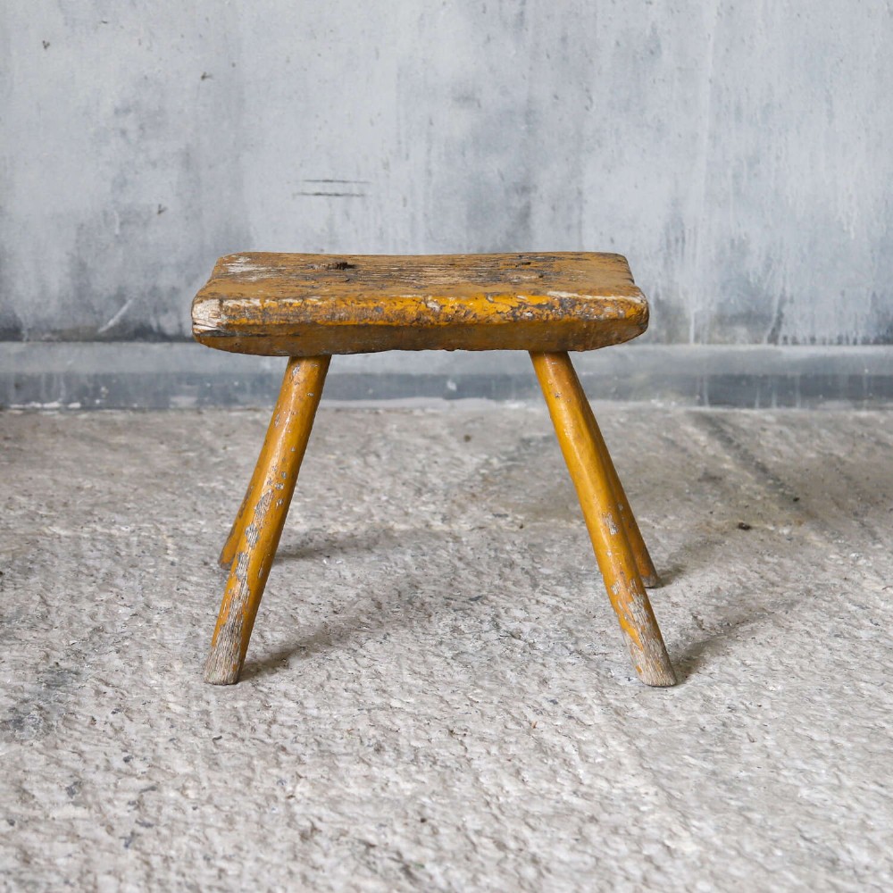 A nineteenth-century rectangular wooden milking stool with four splayed legs and a weathered ochre yellow painted finish. View II