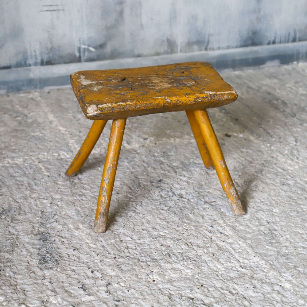A nineteenth-century rectangular wooden milking stool with four splayed legs and a weathered ochre yellow painted finish. View III