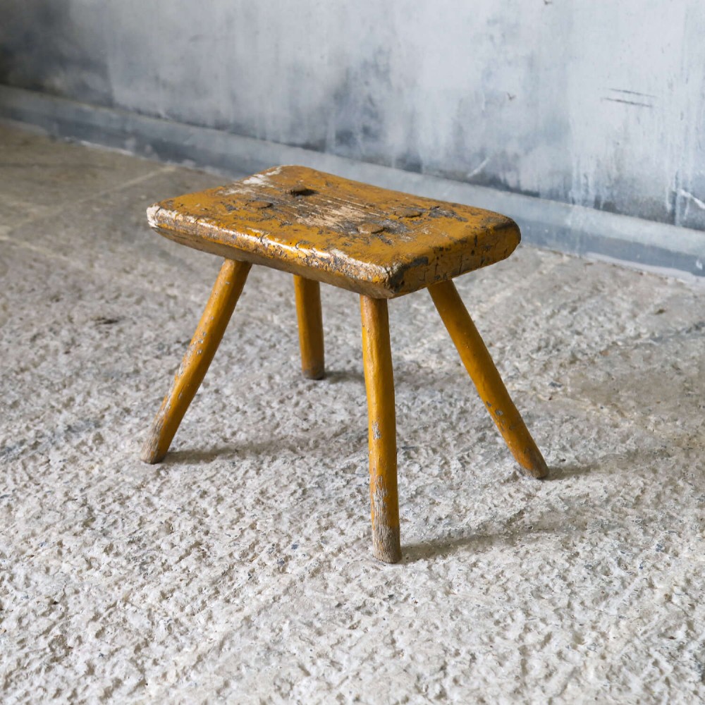 A nineteenth-century rectangular wooden milking stool with four splayed legs and a weathered ochre yellow painted finish. View IV