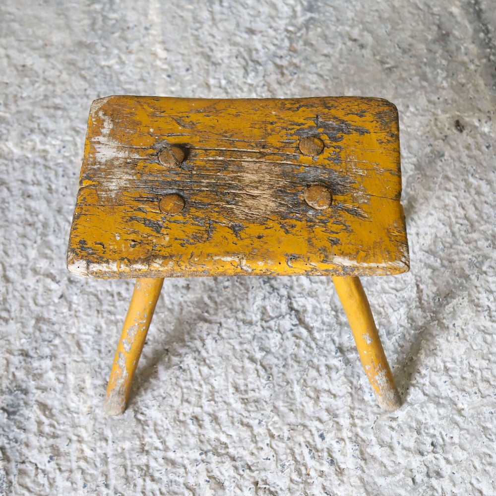 A nineteenth-century rectangular wooden milking stool with four splayed legs and a weathered ochre yellow painted finish. View V