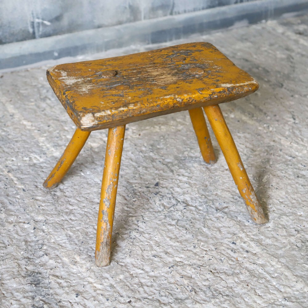 A nineteenth-century rectangular wooden milking stool with four splayed legs and a weathered ochre yellow painted finish. View VI
