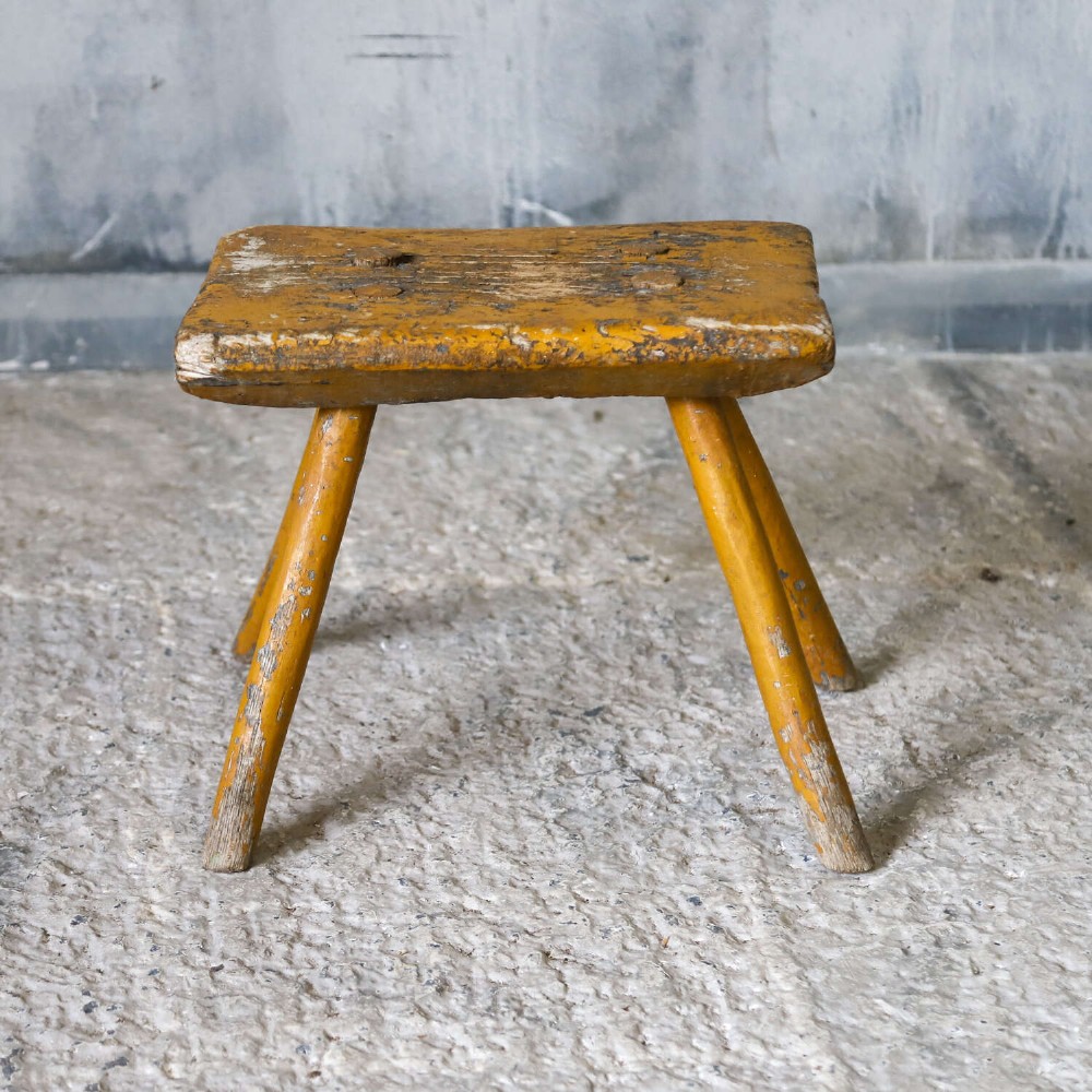 A nineteenth-century rectangular wooden milking stool with four splayed legs and a weathered ochre yellow painted finish. View VII