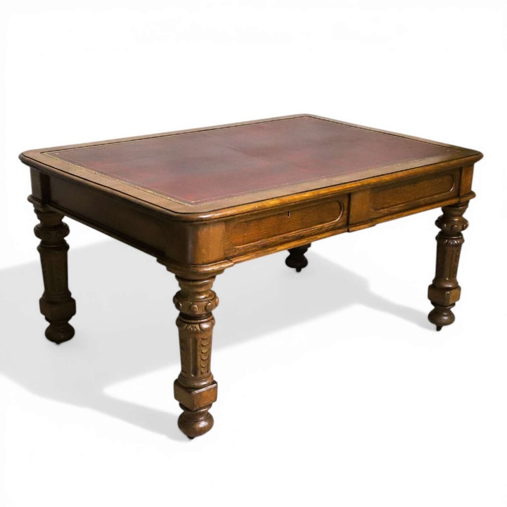 A 19th-century English oak Gothic Revival library table featuring an inset leather top and carved turned legs on brass castors.