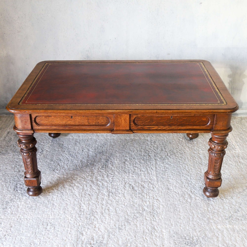 A 19th-century English oak Gothic Revival library table featuring an inset leather top and carved turned legs on brass castors. View II