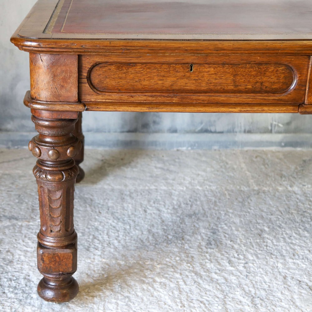 A 19th-century English oak Gothic Revival library table featuring an inset leather top and carved turned legs on brass castors. View III