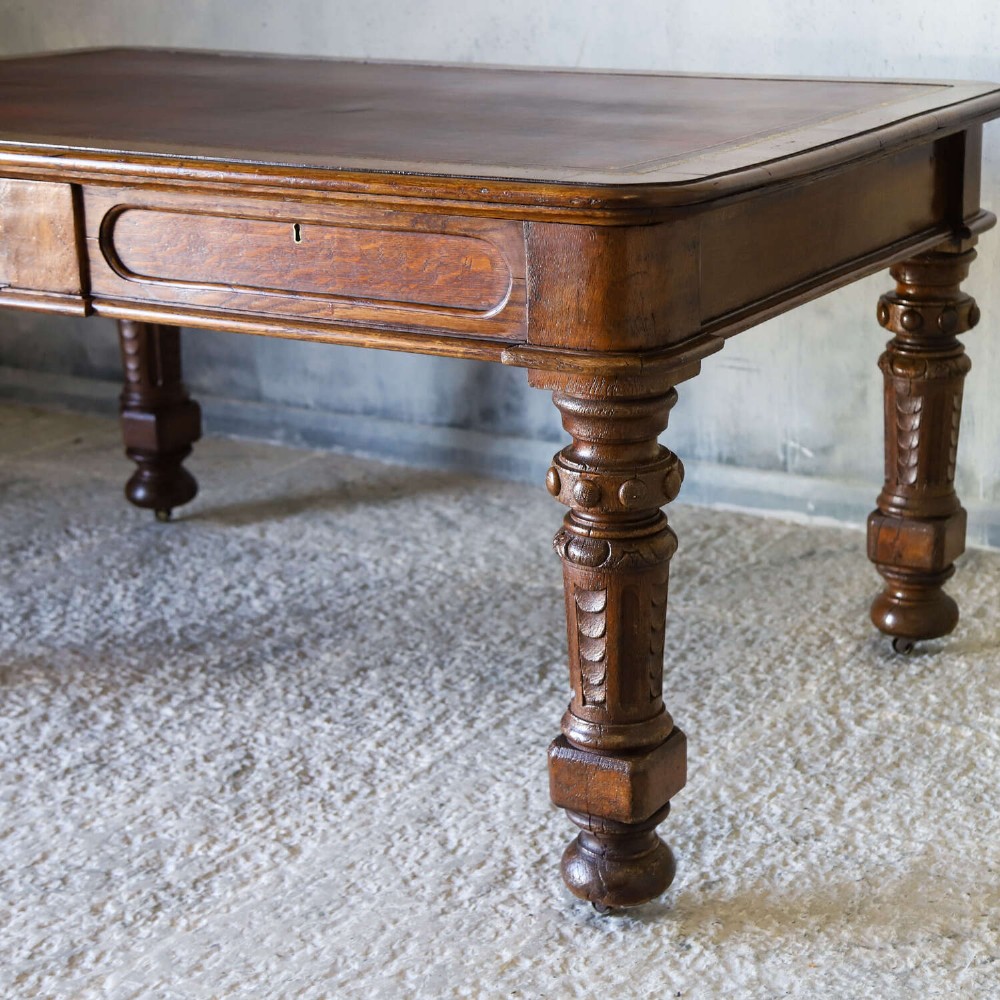 A 19th-century English oak Gothic Revival library table featuring an inset leather top and carved turned legs on brass castors. View IV