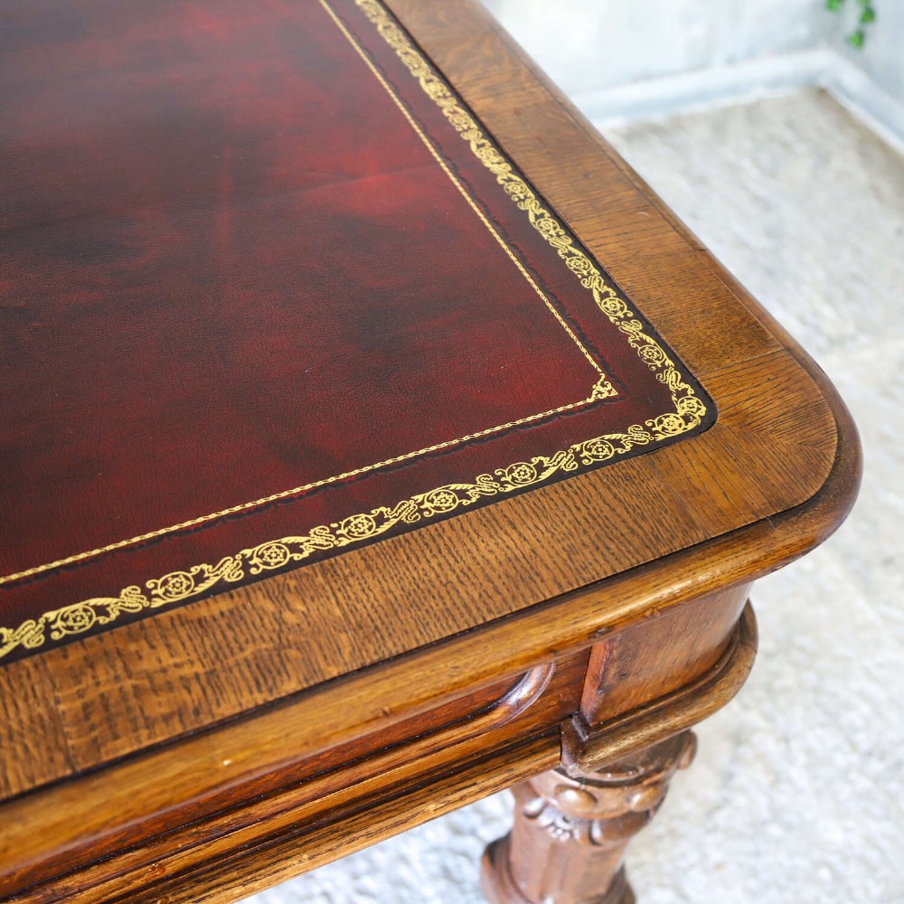 A 19th-century English oak Gothic Revival library table featuring an inset leather top and carved turned legs on brass castors. View V